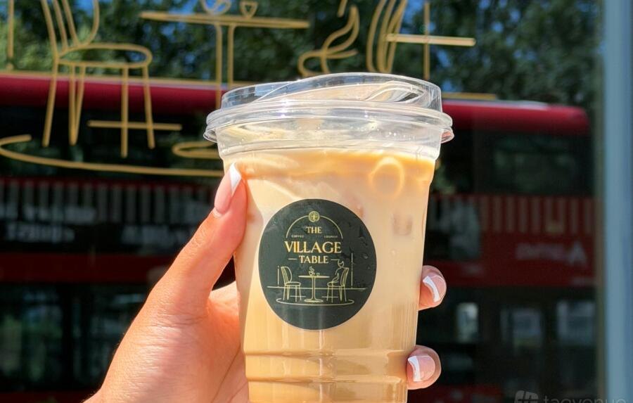 The Village Table iced coffee cup held up against the Croydon skyline